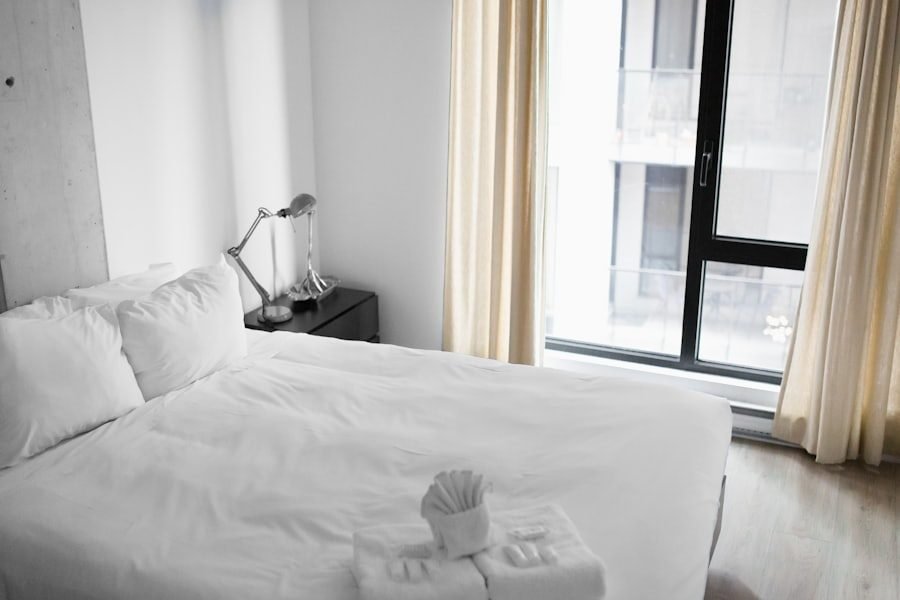Freshly made white bed beside a closed bedroom window in natural light