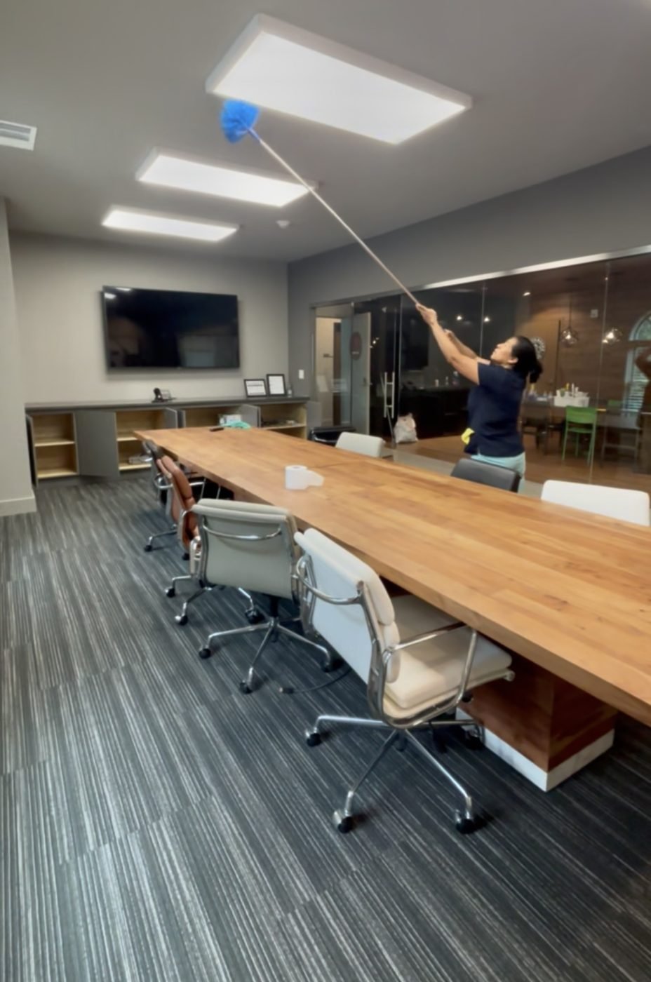 A Starbiz cleaner using an extended duster on the lights above a long conference room table