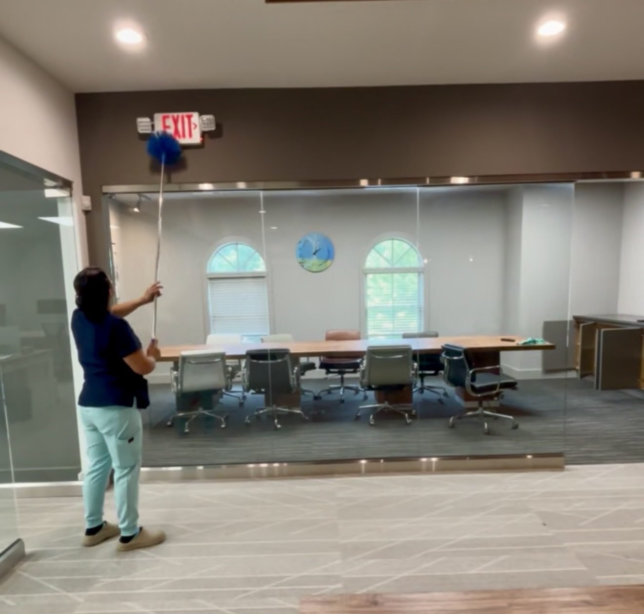 A Starbiz cleaner using an extended duster outside a glass-walled conference room